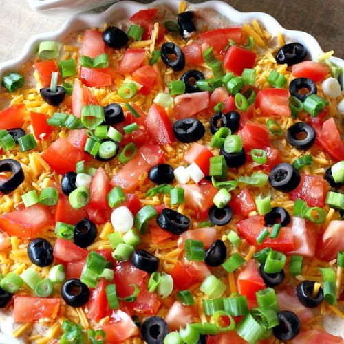 Seven Layer Tex-Mex Dip | Can't Stay Out of the Kitchen | this awesome #TexMex #dip is out of this world. It's terrific for any kind of company or #holiday party. We like it for #tailgating parties & potlucks. Also great for summer #holidays like #FourthOfJuly. #GlutenFree #Mexican #TexMexDip #LayeredMexicanDip #RefriedBeans #Jalapenos #Olives #CheddarCheese #Guacamole #TortillaChips #tomatoes #Avocados #SevenLayerTexMexDip #appetizer #TexMexAppetizer