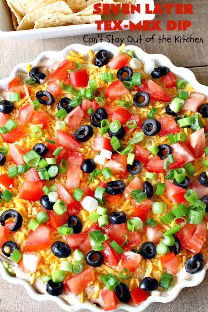 Seven Layer Tex-Mex Dip | Can't Stay Out of the Kitchen | this awesome #TexMex #dip is out of this world. It's terrific for any kind of company or #holiday party. We like it for #tailgating parties & potlucks. Also great for summer #holidays like #FourthOfJuly. #GlutenFree #Mexican #TexMexDip #LayeredMexicanDip #RefriedBeans #Jalapenos #Olives #CheddarCheese #Guacamole #TortillaChips #tomatoes #Avocados #SevenLayerTexMexDip #appetizer #TexMexAppetizer