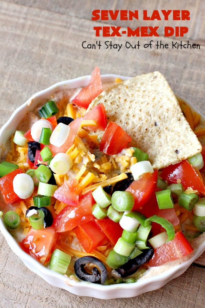 Seven Layer Tex-Mex Dip | Can't Stay Out of the Kitchen | this awesome #TexMex #dip is out of this world. It's terrific for any kind of company or #holiday party. We like it for #tailgating parties & potlucks. Also great for summer #holidays like #FourthOfJuly. #GlutenFree #Mexican #TexMexDip #LayeredMexicanDip #RefriedBeans #Jalapenos #Olives #CheddarCheese #Guacamole #TortillaChips #tomatoes #Avocados #SevenLayerTexMexDip #appetizer #TexMexAppetizer